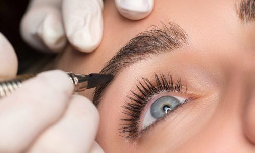 Permanent eyebrow makeup. Cosmetologist applying tattooing of eyebrows. Close up shoot.